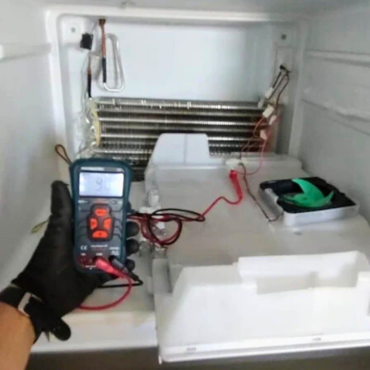 Técnico especializado utilizando multímetro para testar sensores e resistência interna de refrigerador.