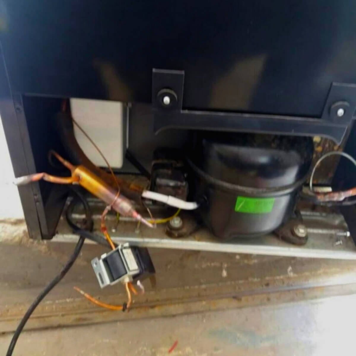 Reparo técnico em compressor e componentes elétricos na parte traseira de equipamento de refrigeração comercial.