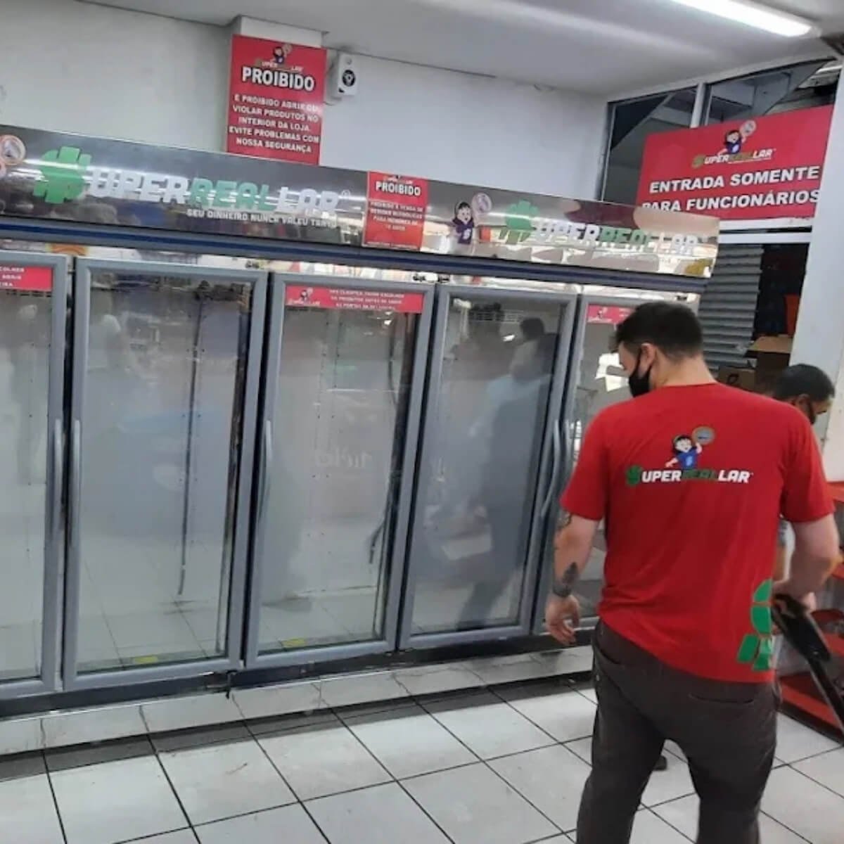 Geladeira expositora comercial de auto serviço com 5 portas de vidro em supermercado recebendo manutenção técnica em Curitiba.