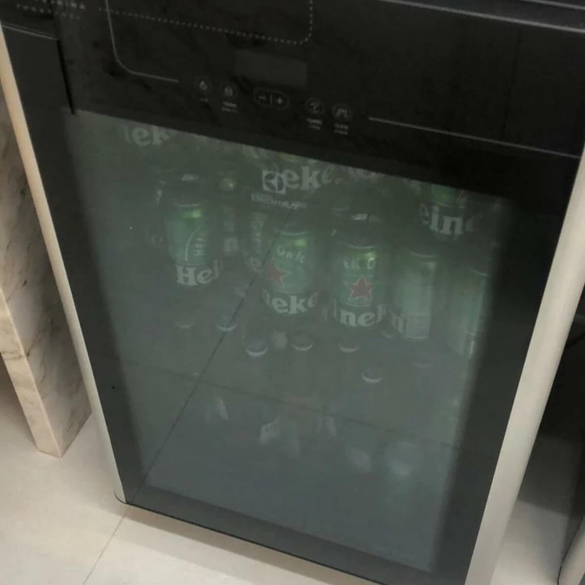 Frigobar preto tipo cervejeira com porta de vidro abastecido com bebidas geladas, ilustrando manutenção de frigobares em Curitiba com foco em silêncio e eficiência.r